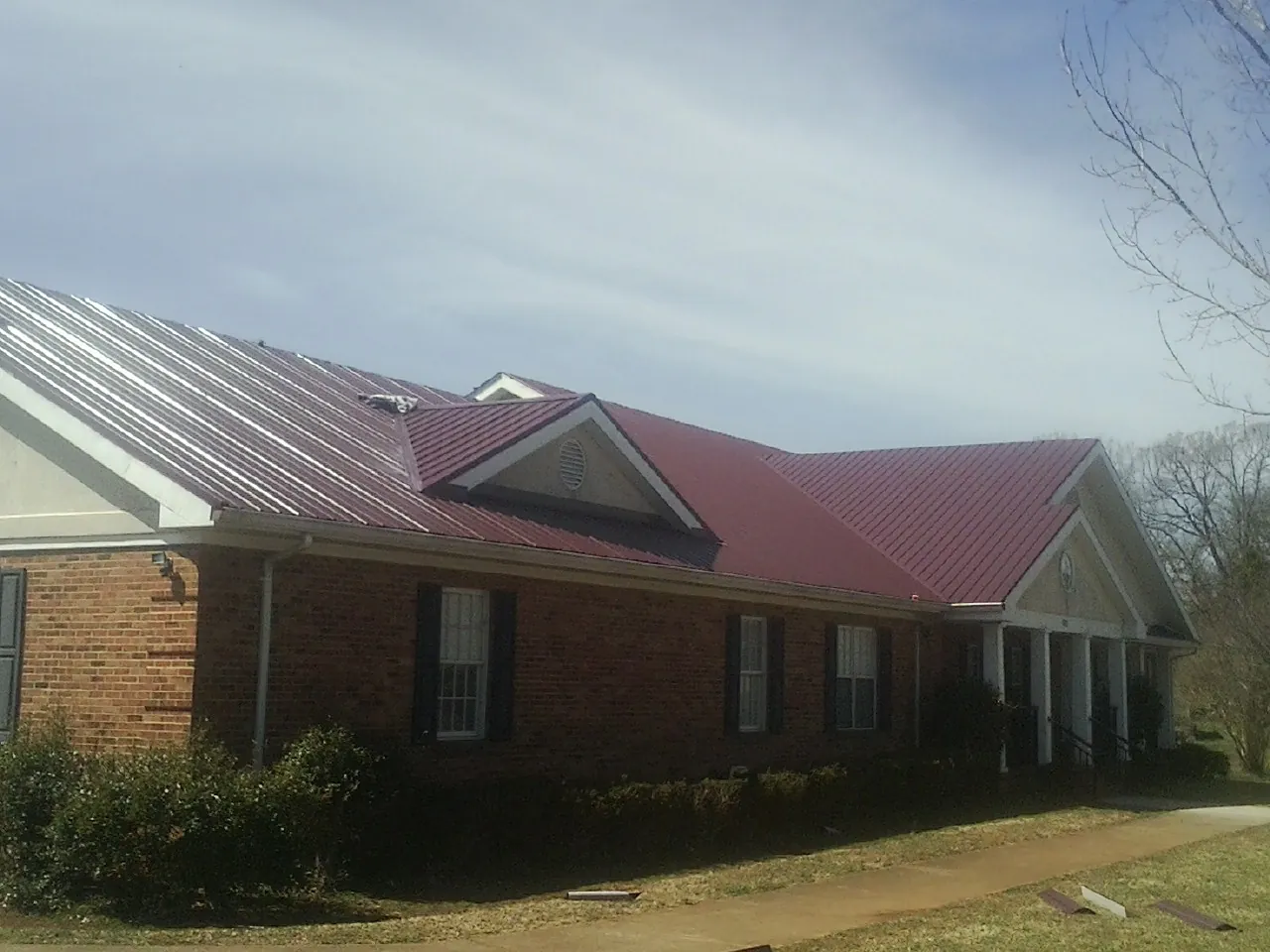 Red metal roof with gabled entries on a long brick building, from a Hail Damage Roof Repair job in Chestertown