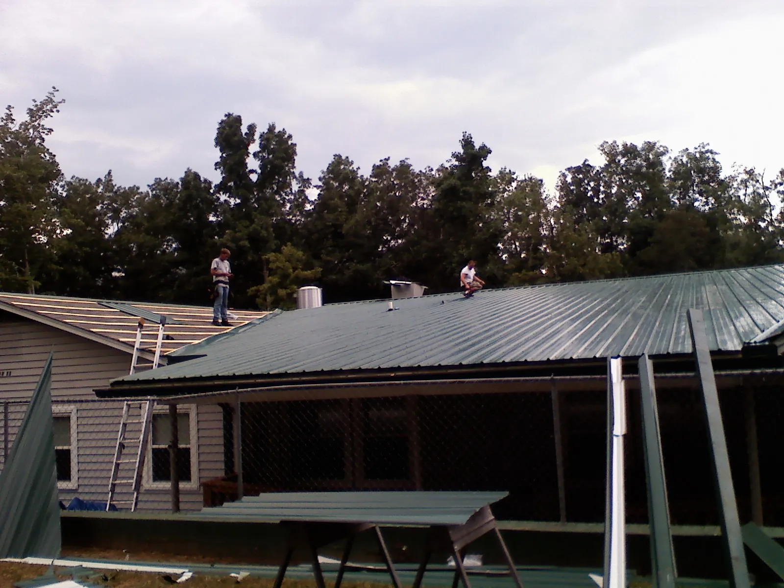 Two roofers installing green metal panels above a covered porch in Chestertown