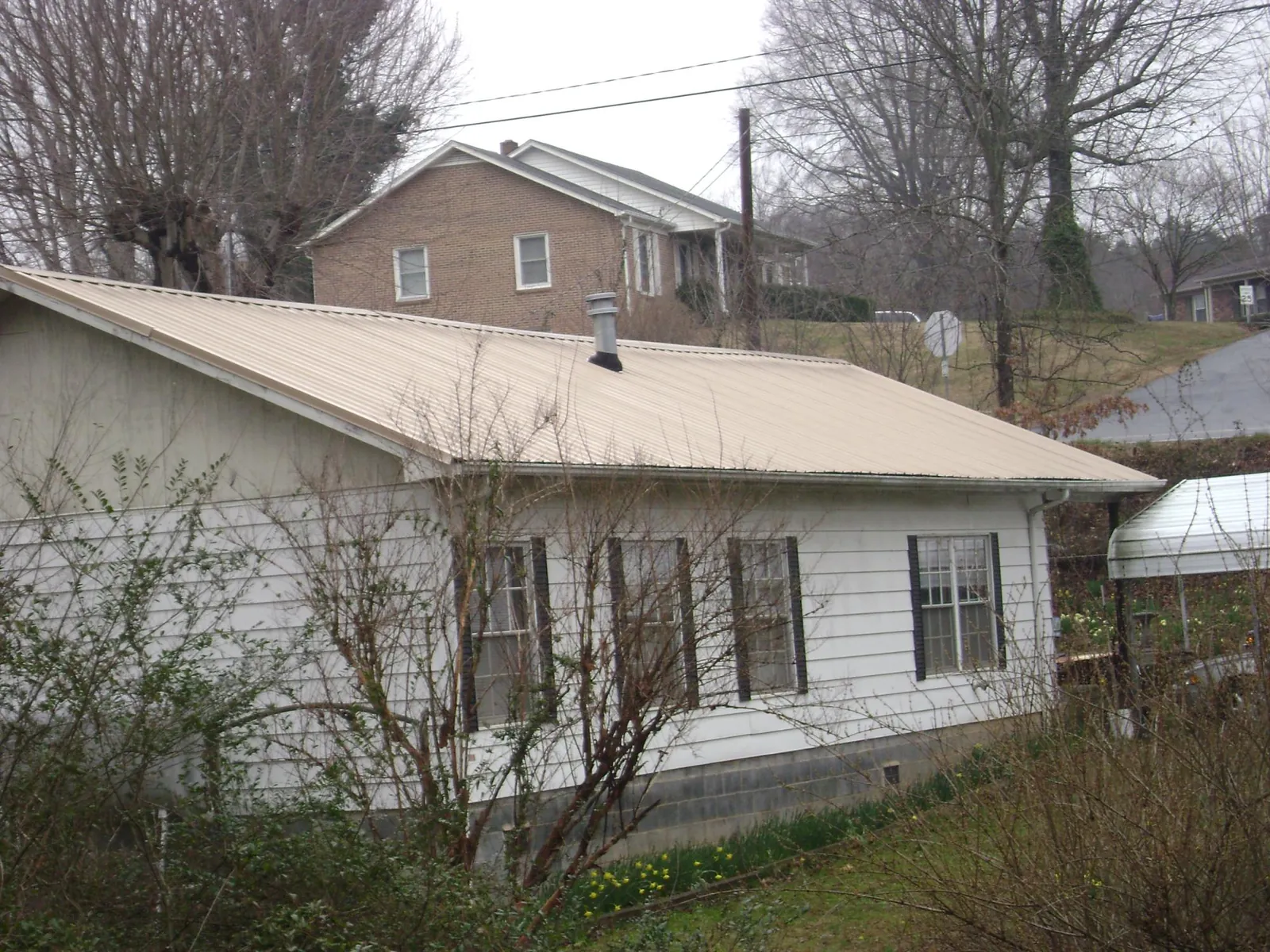 Tan metal roof on a white sided house set into a hillside — Commercial Roofing by Roofing Brothers in Chestertown